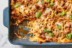 a casserole dish with meat, cheese and spinach leaves on the side