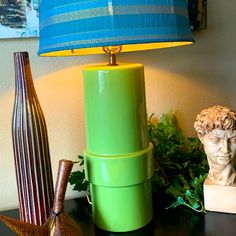 a green lamp sitting on top of a table next to a vase and a busturine