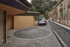 a car parked in front of a building on a cobblestone driveway with a wooden fence around it