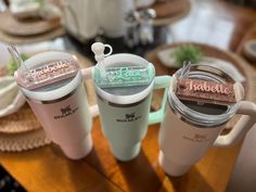 three travel mugs sitting next to each other on top of a wooden table with plates and utensils