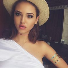 a woman wearing a white shirt and hat posing for the camera with her hands on her hips