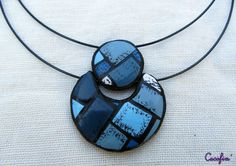 two circular pendants with blue and black designs on a leather cord necklace that is attached to a white cloth