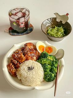 a white plate topped with rice, broccoli and chicken next to a drink