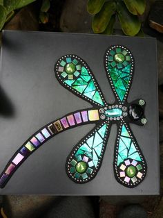 a dragonfly made out of stained glass sitting on top of a black piece of paper