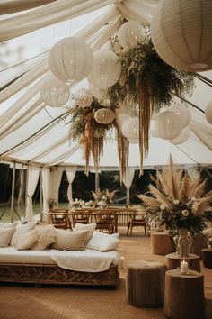 the inside of a tent decorated with white lanterns and hanging plants, pillows and other decorations