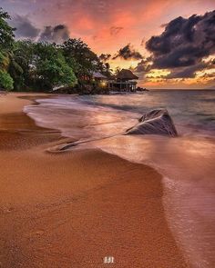 the sun is setting over an ocean beach with waves crashing on it and houses in the distance