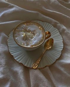 a cup and saucer on a white cloth with gold spoons in the middle