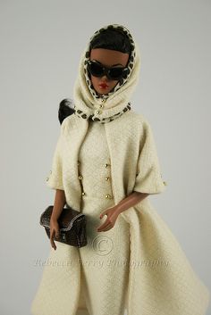 a doll wearing a white coat and black sunglasses with a handbag on her shoulder