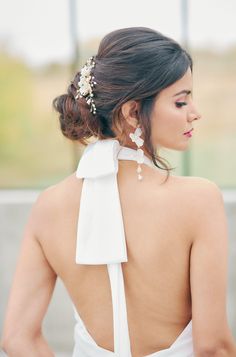 the back of a woman wearing a white dress with a flower in it's hair