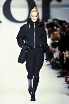 a model walks down the runway in a black coat and matching knee - high boots