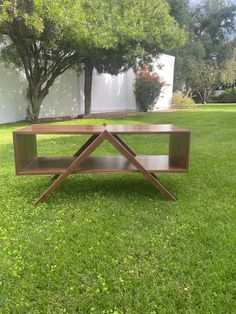 a wooden table sitting in the middle of a grass covered field with trees behind it