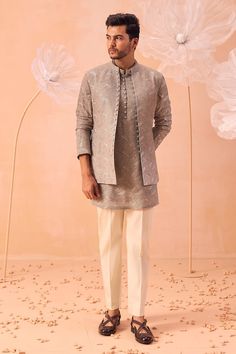 a man standing in front of flowers wearing a gray shirt and white pant suit