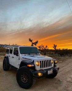 a white jeep parked on top of a dirt road next to a joshua tree at sunset