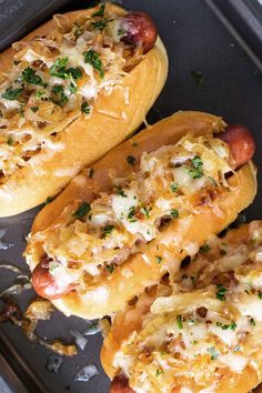 two hot dogs covered in cheese and toppings on a baking sheet with tongs