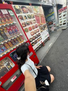 a woman sitting on the ground in front of a vending machine