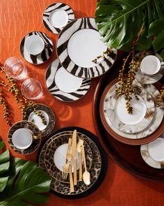 the table is set with zebra print plates and silverware, gold rimmed cutlery, and green leaves