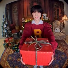 a man holding a red present box in front of a christmas tree