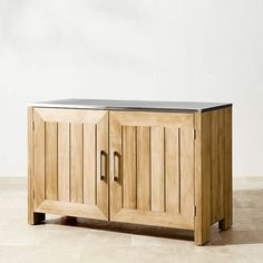 a wooden cabinet sitting on top of a floor next to a white wall with a black metal top