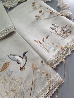 two pieces of embroidered linen with birds and flowers on them, sitting next to each other