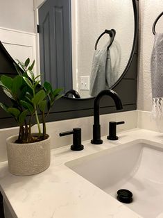 a bathroom sink with two black faucets and a round mirror