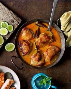 some food is in a pan on a table with limes and spoons next to it