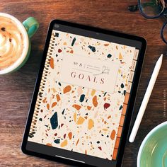 a tablet with the words goals on it next to a cup of coffee and eyeglasses