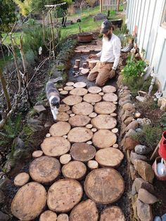 a woman sitting on the side of a building next to a pile of logs and a cat