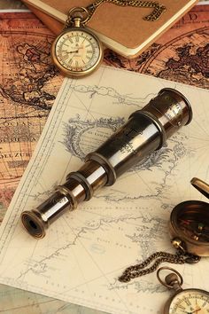 an antique telescope and pocket watch are on top of a map with compasses nearby