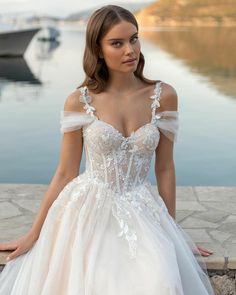 a woman in a white wedding dress sitting on the edge of a body of water