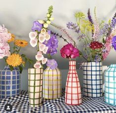 four vases with flowers in them sitting on a checkered tablecloth covered table