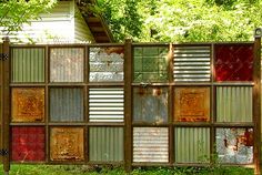 a fence made out of old windows in the grass with trees and bushes behind it