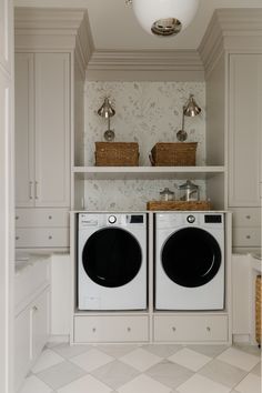 a washer and dryer in a white laundry room with wall - to - wall cabinets