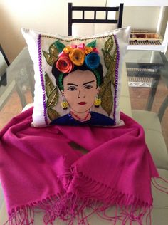 a decorative pillow on top of a chair with a pink scarf around it and an embroidered frilly