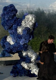 two people standing next to a large blue and silver sculpture