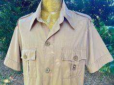 A fun 1980's vintage men's short sleeve safari shirt. The shirt is a light khaki-beige colour and features classic safari shirt details. It has short sleeves, an exaggerated collar and large buttons down the front. The front has four pleated patch pockets with button-down flaps. The shoulders have button down epaulets.  There are short side splits at the hem.  Size Extra Large Measurements: Chest:  124.5 cm / 49 inches Shoulder: 51 cm / 20 inches Length: 78.5 cm / 31 inches Sleeve: 24.5 cm / 9.7 Vintage Safari, Safari Shirt, Beige Colour, Large Buttons, 1980s Vintage, Guys And Girls, Beige Color, Men Short Sleeve, Vintage Men