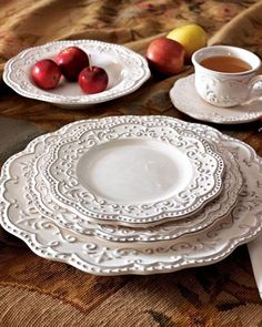 a table topped with white plates and cups filled with fruit on top of a cloth covered table