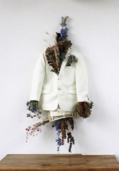 a white jacket with dried flowers hanging from it's lapel on a wall