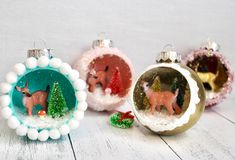 three christmas ornaments sitting on top of a white wooden table next to each other and one has an ornament in the shape of a deer