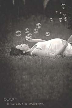 a woman laying in the grass blowing bubbles