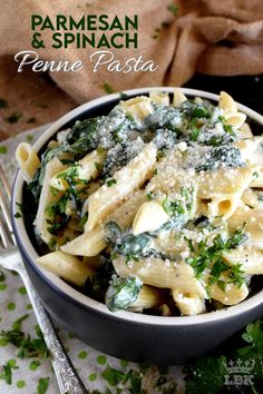 a bowl filled with pasta and spinach on top of a table next to silverware