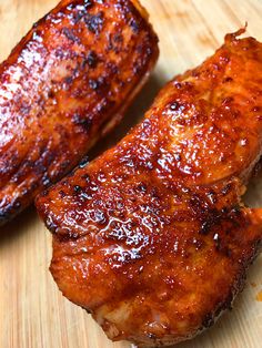 two pieces of meat sitting on top of a wooden cutting board next to each other