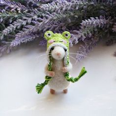 a small stuffed animal with a hat and scarf on it's head standing in front of purple flowers