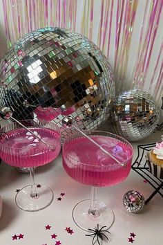 two pink cocktails in front of disco balls and cupcakes on a table