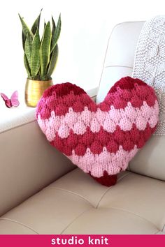 a crocheted heart sitting on top of a couch next to a potted plant