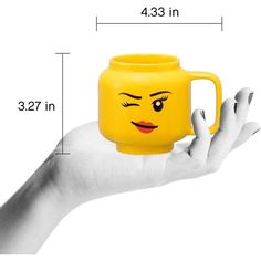 a hand holding a yellow mug with a face drawn on it