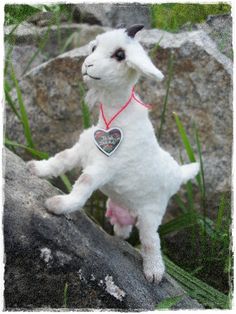 a stuffed lamb with a heart on it's collar is standing on a rock