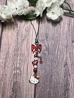 a hello kitty necklace with red beads and white flowers on a wooden table next to it