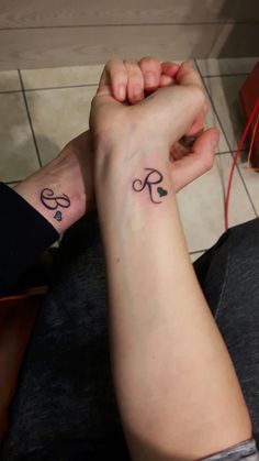 two people holding hands with tattoos on their wrists and wristbands, one has the letter k in cursive writing