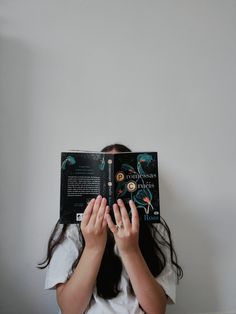 a girl is hiding her face behind a book