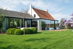 the house is surrounded by lush green grass and purple lilacs in front of it